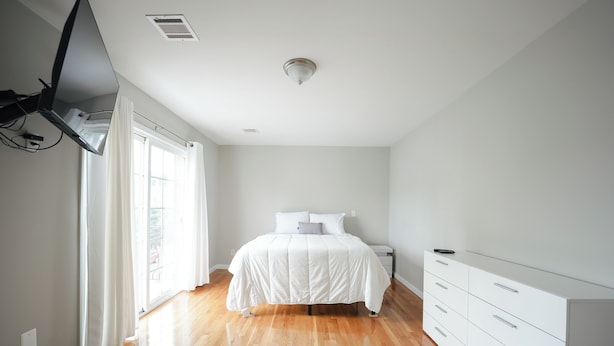 A bedroom with a bed, a dresser, and a window with curtains. - Newark Liberty Gem Brick House - Apt 3 (Newark)