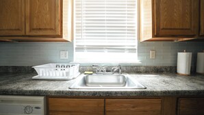 A kitchen with wooden cabinets, a granite countertop, a stainless steel sink, and a window with blinds. - Newark Liberty Gem Brick House - Apt 3 (Newark)