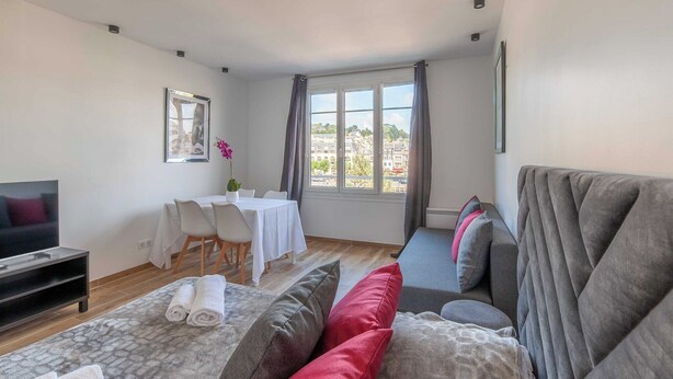 Una sala de estar moderna con un sofá, un televisor, una mesa de comedor con sillas y un ventanal grande con cortinas.