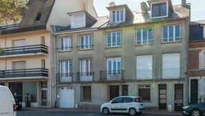 Un edificio de varios pisos con balcones, una camioneta blanca estacionada al frente y un automóvil en la calle.