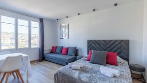 Una habitación de hotel moderna con cama, sofá, mesa de comedor y grandes ventanales con vistas a la ciudad.