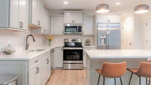 Una cocina moderna con armarios blancos, electrodomésticos de acero inoxidable y una isla central con dos sillas.