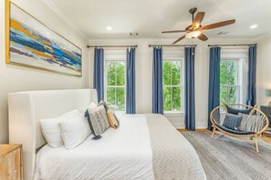 A bedroom with a large bed, a ceiling fan, and a rattan chair.