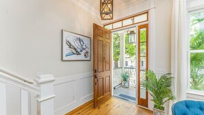 Un pasillo con una puerta de madera, una obra de arte enmarco, una planta en maceta y un sillón azul.
