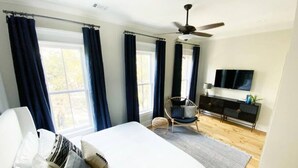 A bedroom with a large bed, a chair, a TV, and a ceiling fan. - Magnolia Estate – 3 Private Quarters, Walk to Sites (Savannah)