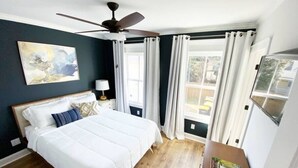 A bedroom with a bed, a ceiling fan, a nightstand, a lamp, and a window with curtains.