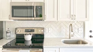 A kitchen with white cabinets, a stainless steel microwave, a stove, and a sink.