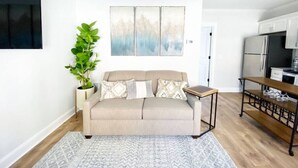 A living room with a beige sofa, a coffee table, a potted plant, and a painting on the wall.