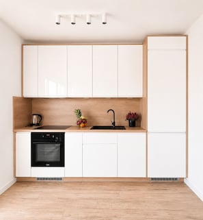 Une cuisine moderne avec des meubles blancs, un four noir, un évier et un plan de travail en bois.