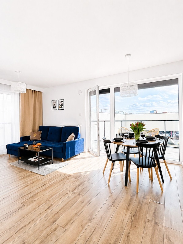 Un salon moderne avec un canapé bleu, une table à manger avec des chaises et de grandes fenêtres donnant sur un paysage.