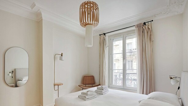 A hotel room with a large bed, a round mirror, a bedside table, a chair, and a window with curtains. - Authentic apartment - 3BR/8P - Clignancourt (Paris)