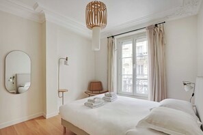 A hotel room with a large bed, a round mirror, a bedside table, a chair, and a window with curtains. - Authentic apartment - 3BR/8P - Clignancourt (Paris)