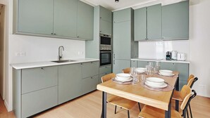 A modern kitchen with grey cabinets, a wooden dining table set for four, and a built-in oven. - Authentic apartment - 3BR/8P - Clignancourt (Paris)