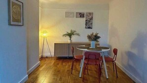 A dining area with a round table, four chairs, a lamp, a plant, and framed pictures on the wall.
