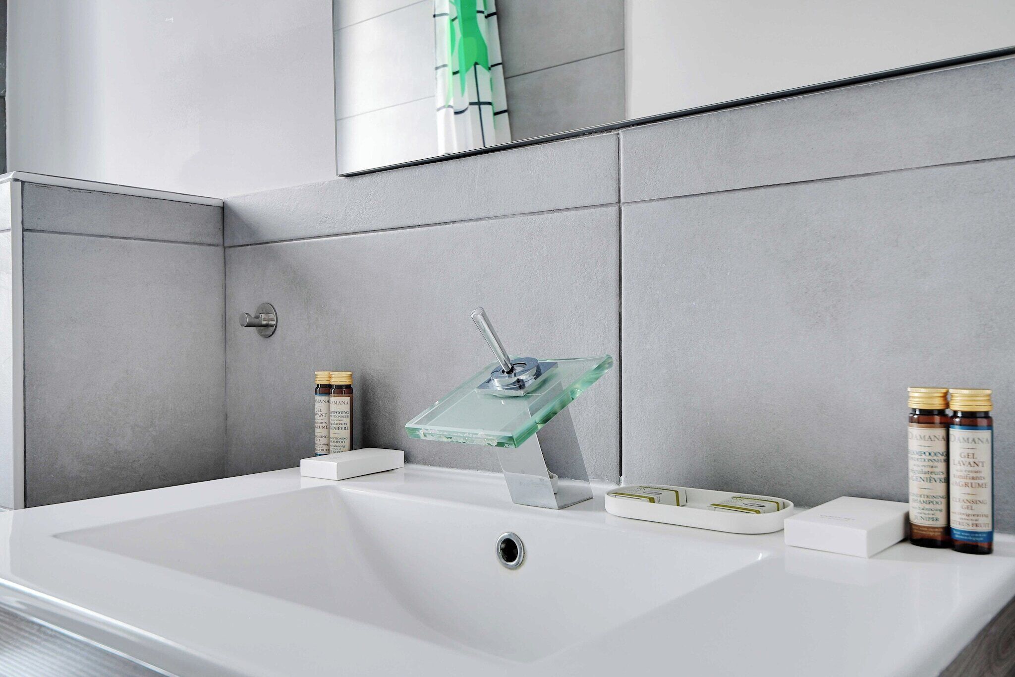 Ein modernes Badezimmer mit einem weißen Waschbecken, einer Seifenschale aus Glas sowie zwei Flaschen Shampoo und Conditioner.