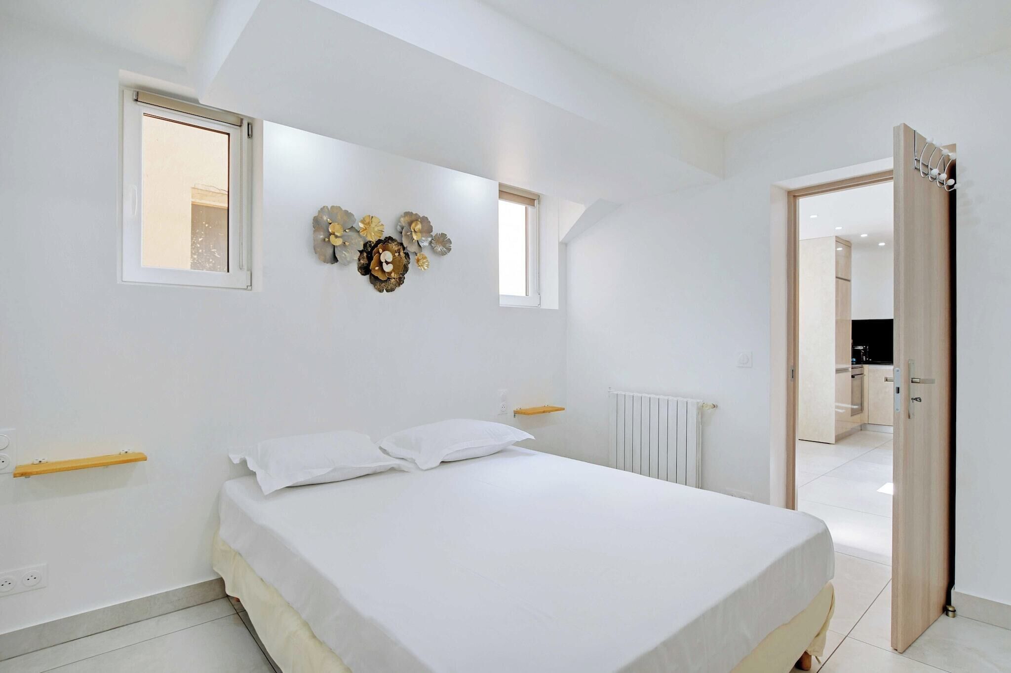 A bedroom with a bed, a window, a radiator, and a door leading to a kitchen.