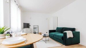 A modern living room with a green sofa, a round wooden dining table, and a TV on a stand. - Comfortable Studio for 2 people - Puteaux (Puteaux)