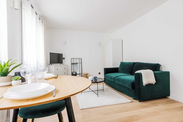 Una sala de estar moderna con un sofá verde, una mesa de comedor redonda de madera y un televisor sobre un mueble bajo.