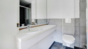 Un baño moderno con lavamanos, espejo y retrete blancos.