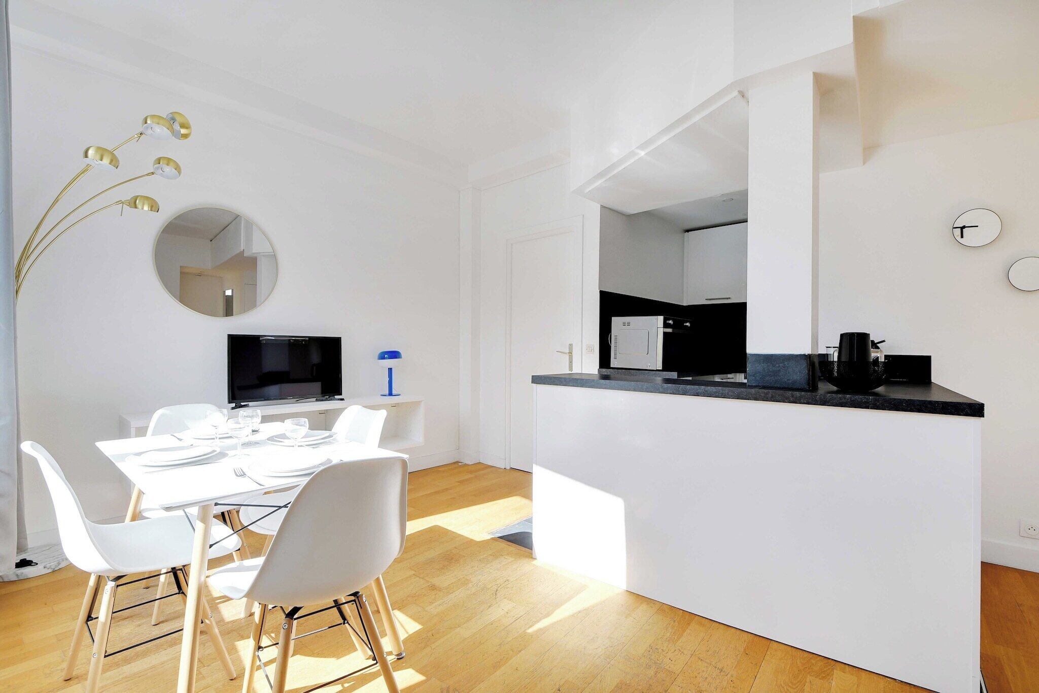 A modern kitchen with a black countertop, white cabinets, and a built-in oven. There is a dining area with a white table and chairs, and a large mirror on the wall.