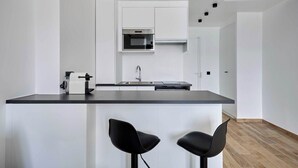 A modern kitchen with white cabinets, a black countertop, and two black bar stools.