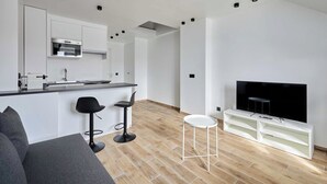 A modern living room with a grey sofa, a small white table, and a TV stand with a flat-screen TV.