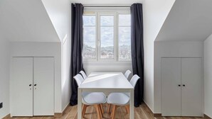 A room with a white table and chairs, a window with curtains, and two white wardrobes.