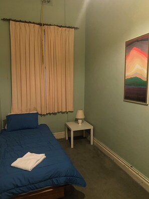 Una camera da letto con un letto, un comodino, una lampada, una finestra con tende e un quadro appeso al muro.