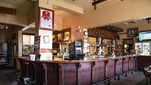 A bar area with a wooden counter, a clock, and various bottles and glasses on shelves. - Culcairn Hotel (Culcairn)