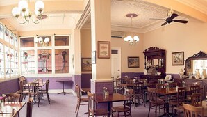 A spacious dining area with multiple wooden tables and chairs, a ceiling fan, and ornate chandeliers. - Culcairn Hotel (Culcairn)