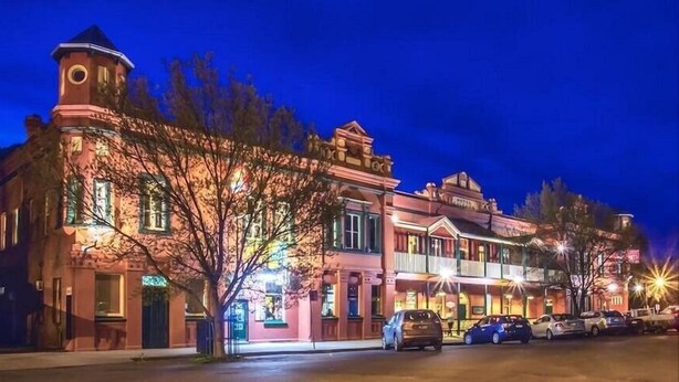 A historic building with a clock tower, multiple stories, and a row of parked cars. - Culcairn Hotel (Culcairn)