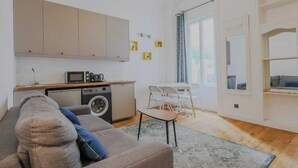 A compact living space with a kitchenette, a sofa, a small dining table, and a washing machine.