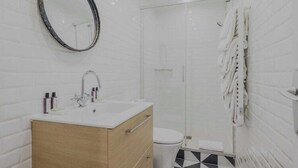A modern bathroom with a wooden vanity, a round mirror, a toilet, and a shower area.