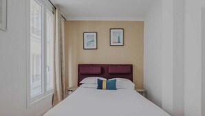 A hotel room with a large bed, two framed pictures on the wall, and a window with curtains.