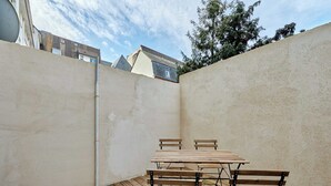 A small outdoor patio area with a wooden table and benches, surrounded by high walls.