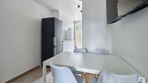 A modern kitchen with white cabinets, a black refrigerator, and a dining area with a white table and grey chairs.