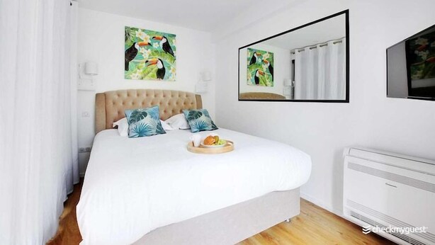 A bedroom with a large bed, white bedding, a breakfast tray, a mirror, and tropical-themed artwork. - Cozy apartment - 1BR/4P Montmartre / Sacré Cœur (Paris)