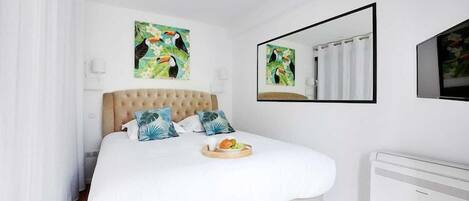 Ein Schlafzimmer mit einem großen Bett, weißer Bettwäsche, einem Frühstücksbrettchen, einem Spiegel und Kunstwerken mit tropischem Motiv.