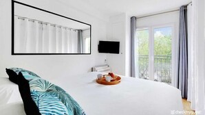 A hotel room with a large bed, a mounted TV, a balcony with curtains, and a breakfast tray on the bed. - Cozy apartment - 1BR/4P Montmartre / Sacré Cœur (Paris)