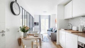 A modern kitchen with white cabinets, a wooden countertop, and a dining area with a table and chairs. - Cozy apartment - 1BR/4P Montmartre / Sacré Cœur (Paris)