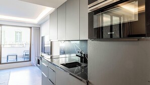 Une cuisine moderne dotée d’un four encastré, d’un évier en acier inoxydable et d’une grande fenêtre donnant sur un balcon.