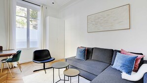 Una sala de estar moderna con un sofá gris, dos mesas redondas, una silla negra y un cuadro abstracto grande en la pared.