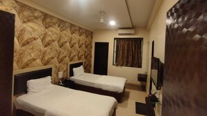 Une chambre d’hôtel avec deux lits simples, un ventilateur de plafond, un appareil de climatisation, une télévision et une fenêtre avec des rideaux.