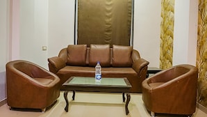 Un canapé en cuir marron, avec une table basse en verre au centre, flanqué de deux fauteuils en cuir. Une bouteille d’eau est posée sur la table.