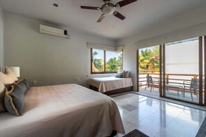 Une chambre d’hôtel avec deux lits, un ventilateur de plafond, une grande fenêtre et un balcon avec des chaises.