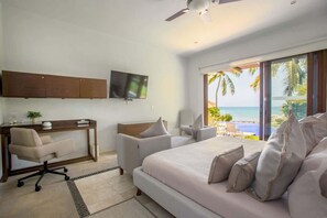 A hotel room with a bed, a desk, a chair, a TV, and a view of the ocean.