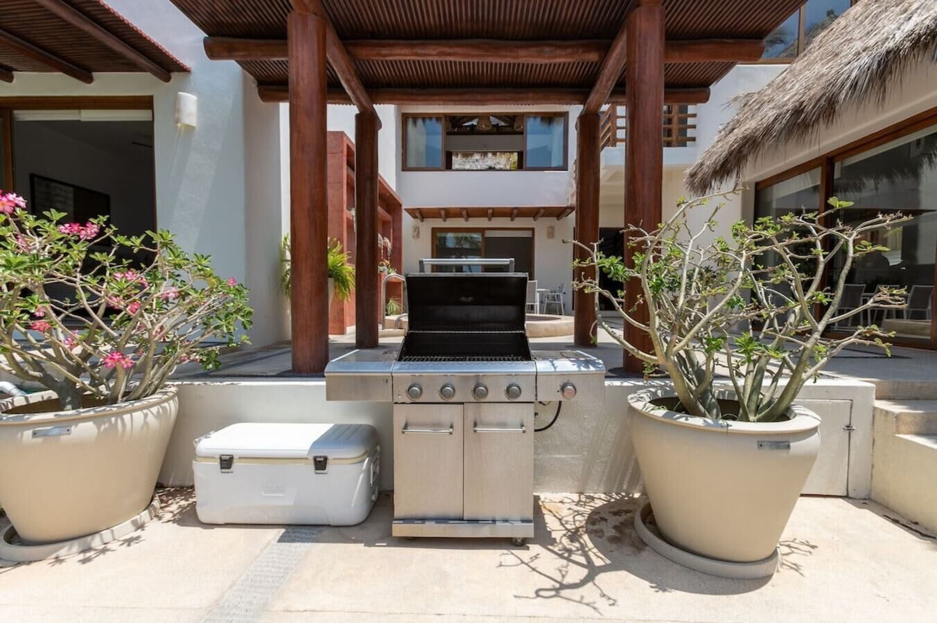 An outdoor grill area with a built-in oven, surrounded by potted plants, under a wooden pergola.