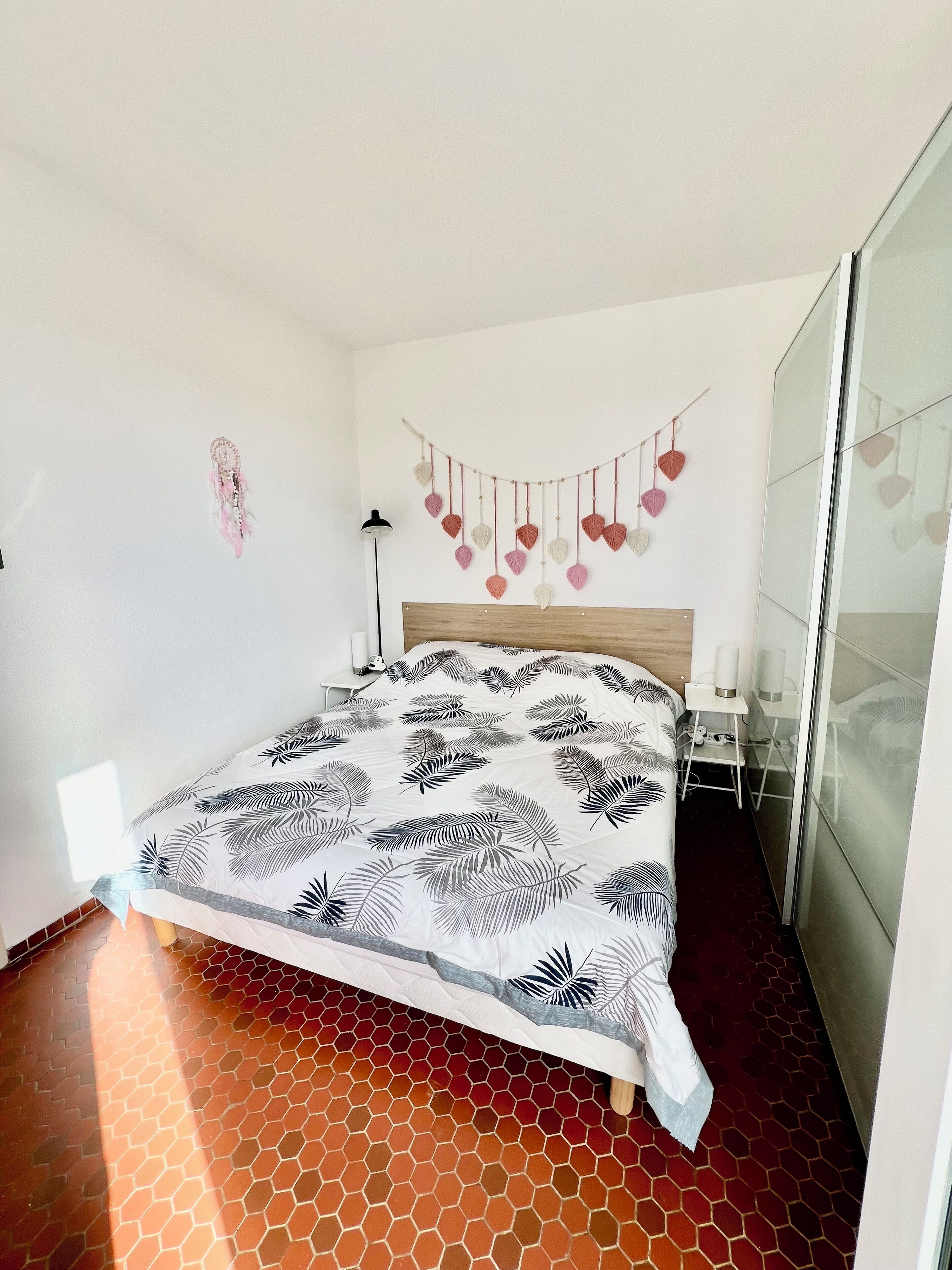A hotel room with a bed, a wall-mounted heart decoration, a bedside table, and a floor with a hexagonal pattern.