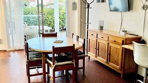 Un comedor con una mesa redonda, sillas, un mueble de madera, un televisor en la pared y un ventilador de techo.