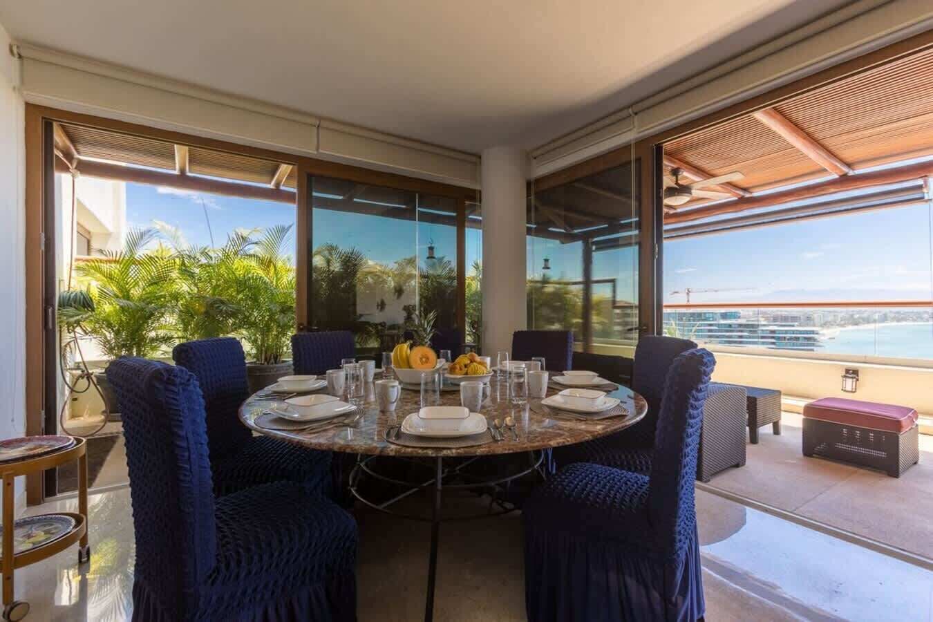 A dining area with a round table, blue chairs, and a view of the ocean.